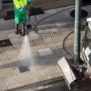 Sweeper washing a street sidewalk with high pressure water jet machine of a cleaning vehicle. Street maintenance