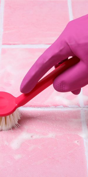 Washing pink tiles in rubber gloves close-up
