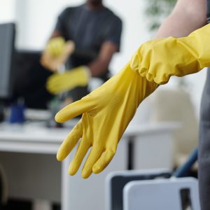 Hands of female worker of contemporary cleaning company putting on yellow protective rubber gloves before mopping floor of office